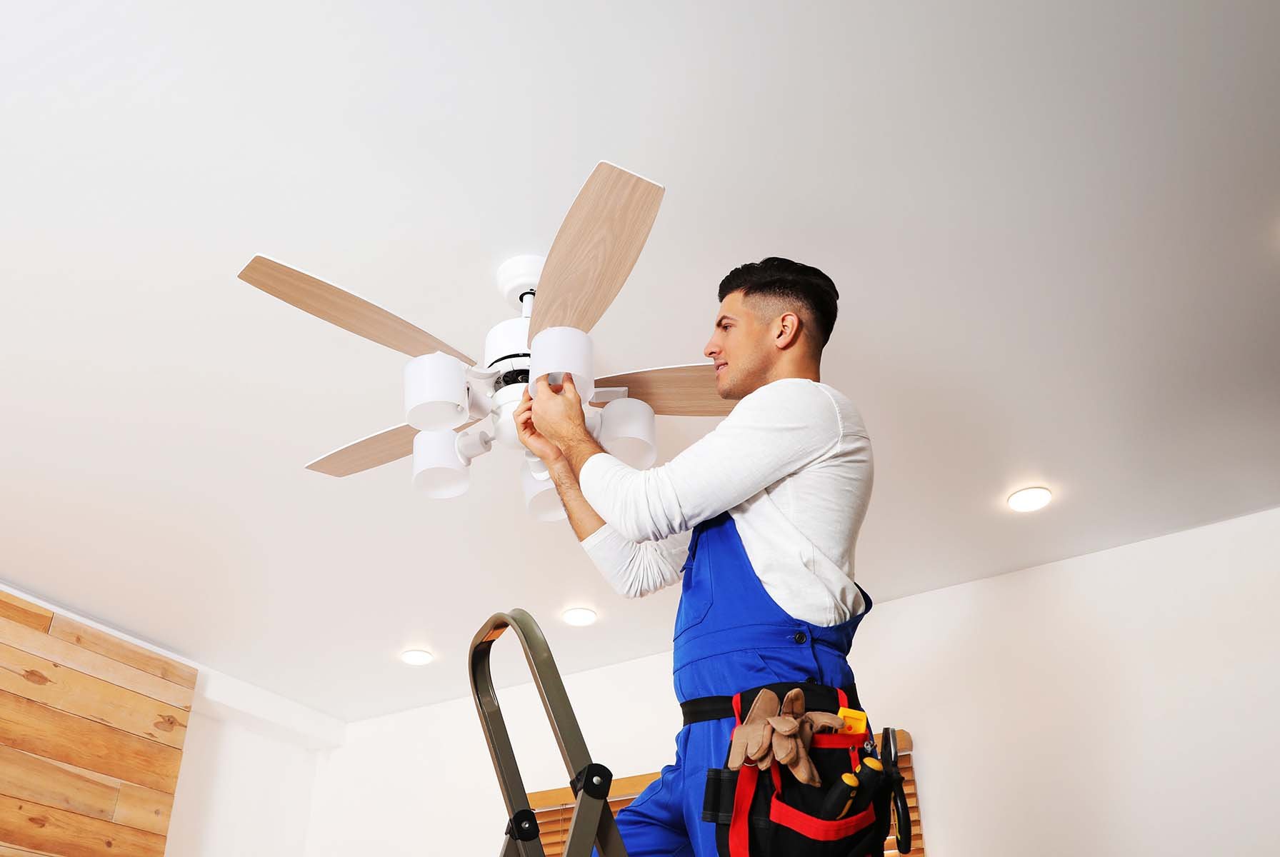 Man on ladder installing a ceiling fan.