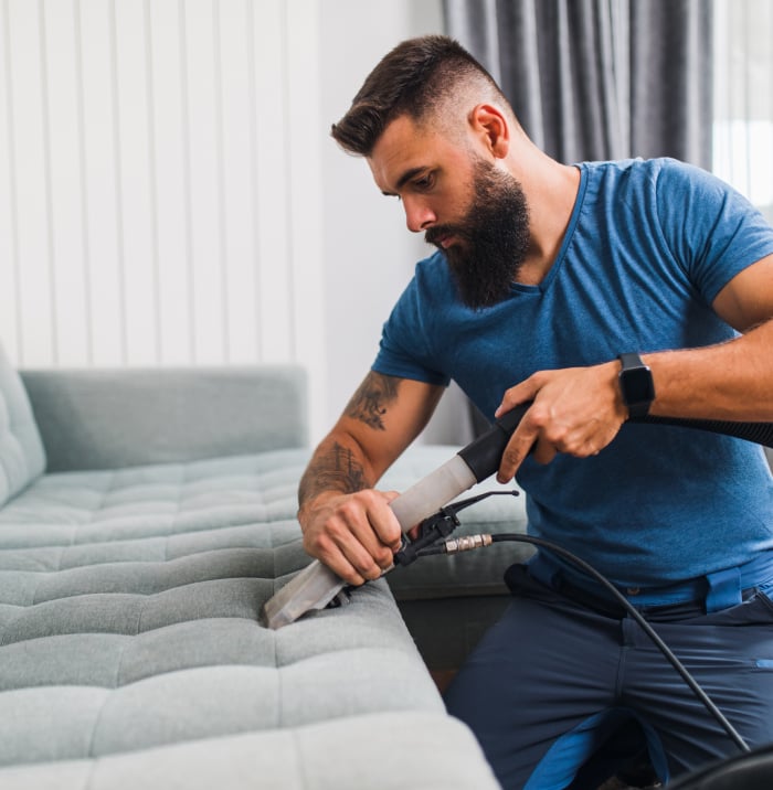 A person vacuuming a sofa cushion