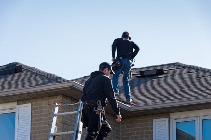 Two people inspecting the roof of a house.