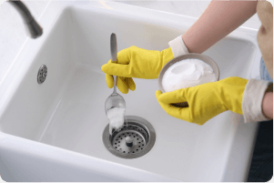 A person putting baking soda in a sink drain.