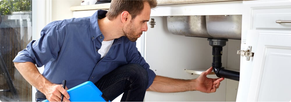 Person inspecting pipe under sink.