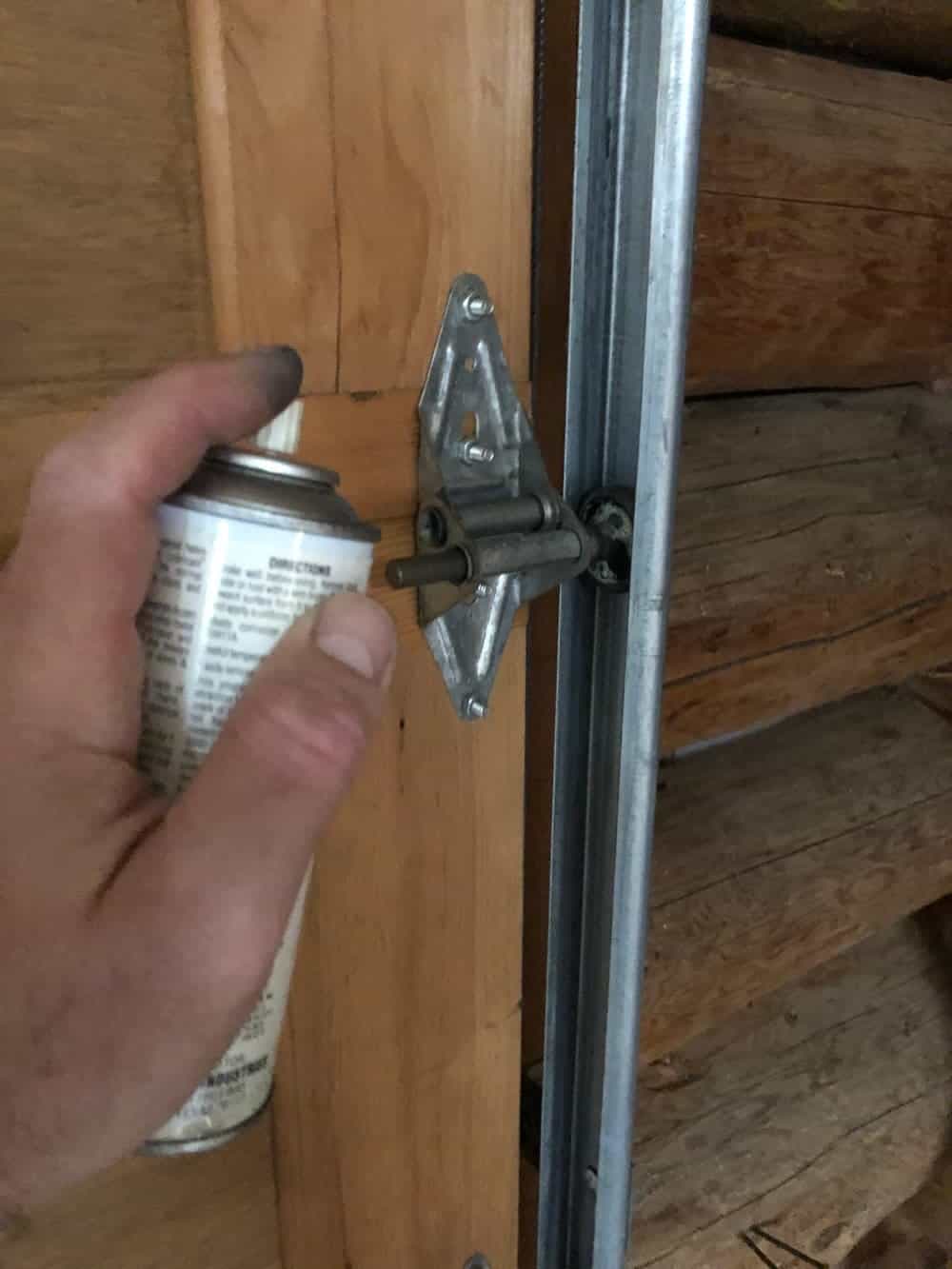 spraying lubricant onto garage door hinge